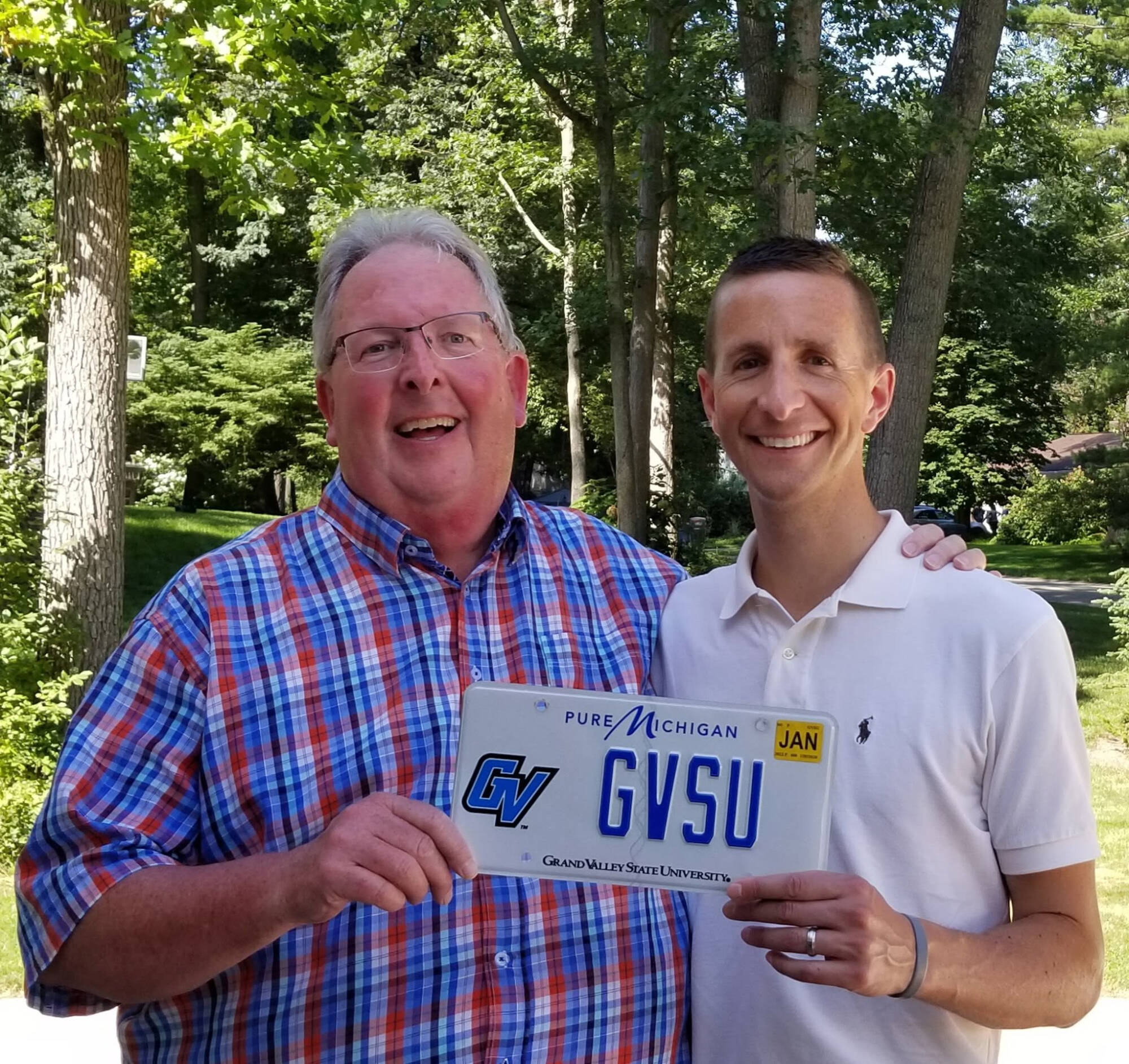 Bob Stoll handing GVSU license plate to his son